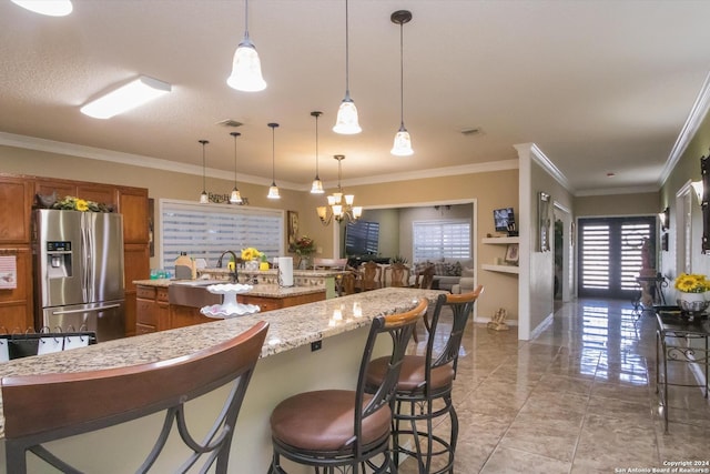 kitchen with brown cabinets, a breakfast bar area, stainless steel refrigerator with ice dispenser, and an island with sink