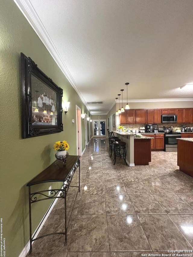 kitchen featuring crown molding, a breakfast bar area, dark countertops, hanging light fixtures, and appliances with stainless steel finishes