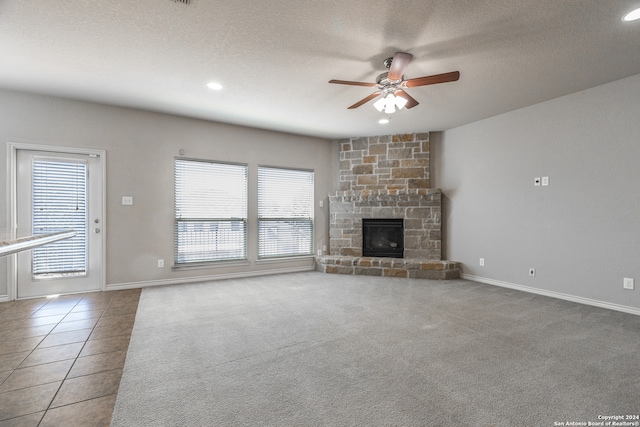 unfurnished living room with a wealth of natural light, tile patterned floors, a stone fireplace, and ceiling fan