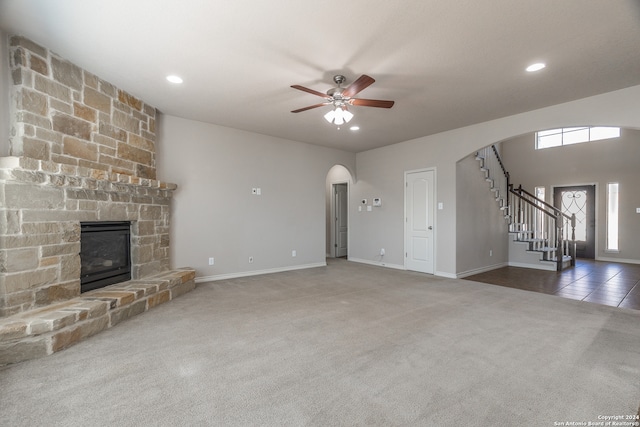 unfurnished living room with ceiling fan, a stone fireplace, and carpet