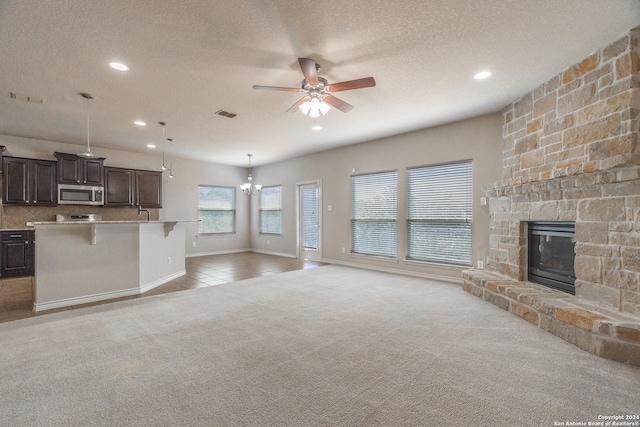 unfurnished living room featuring a textured ceiling, light colored carpet, a fireplace, and ceiling fan