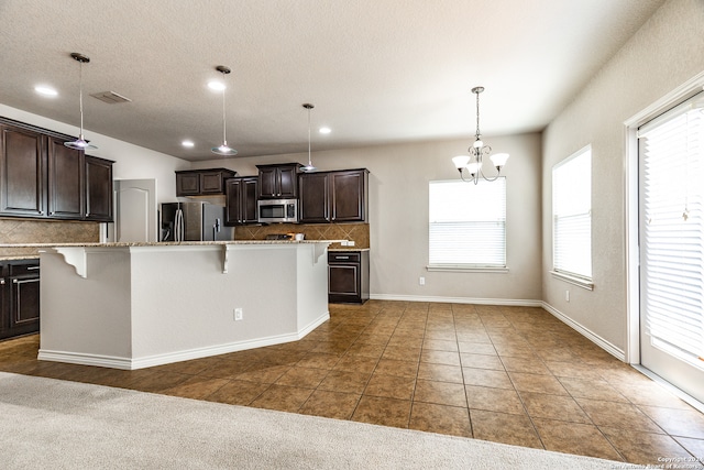 kitchen with a breakfast bar area, hanging light fixtures, stainless steel appliances, a center island with sink, and tasteful backsplash