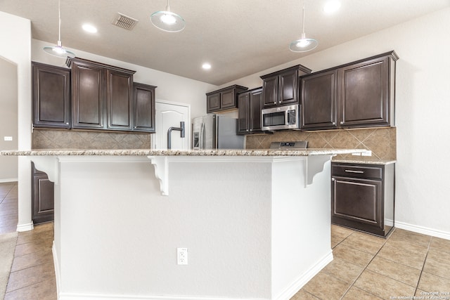 kitchen with appliances with stainless steel finishes, a breakfast bar, an island with sink, and decorative light fixtures