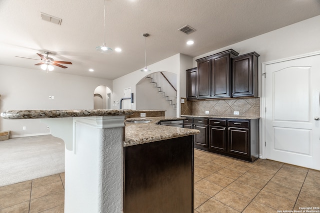 kitchen featuring a breakfast bar area, hanging light fixtures, dark brown cabinets, backsplash, and ceiling fan