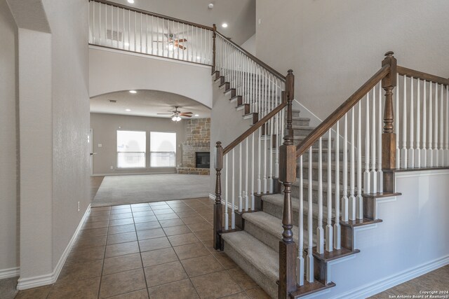 stairs with a towering ceiling, carpet floors, a large fireplace, and ceiling fan