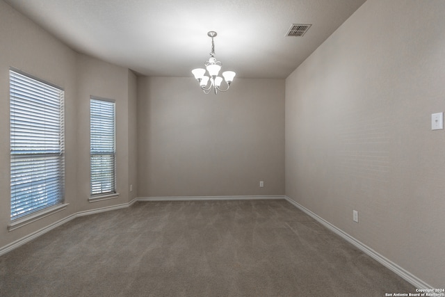 unfurnished room featuring an inviting chandelier, a healthy amount of sunlight, and dark colored carpet