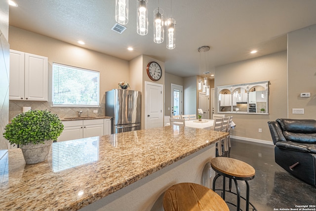 kitchen featuring tasteful backsplash, sink, white cabinets, a kitchen breakfast bar, and stainless steel fridge