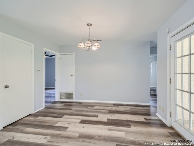 unfurnished room with plenty of natural light, ceiling fan with notable chandelier, and wood-type flooring