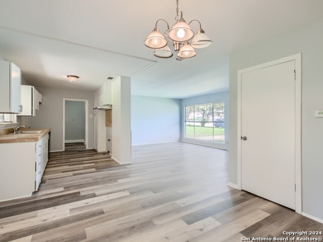 kitchen featuring sink, a notable chandelier, decorative light fixtures, light wood-type flooring, and white cabinetry