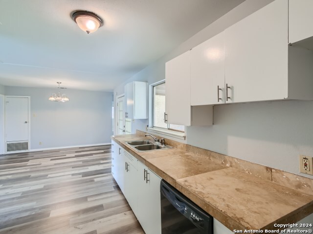 kitchen with white cabinets, light wood-type flooring, hanging light fixtures, and black dishwasher