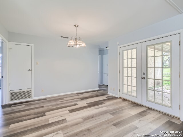 empty room featuring light wood-type flooring, french doors, and an inviting chandelier