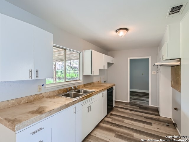 kitchen with sink, dishwasher, white cabinetry, and light wood-type flooring