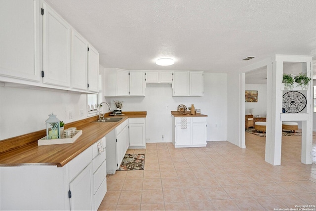 kitchen featuring visible vents, light tile patterned floors, white cabinets, a textured ceiling, and a sink