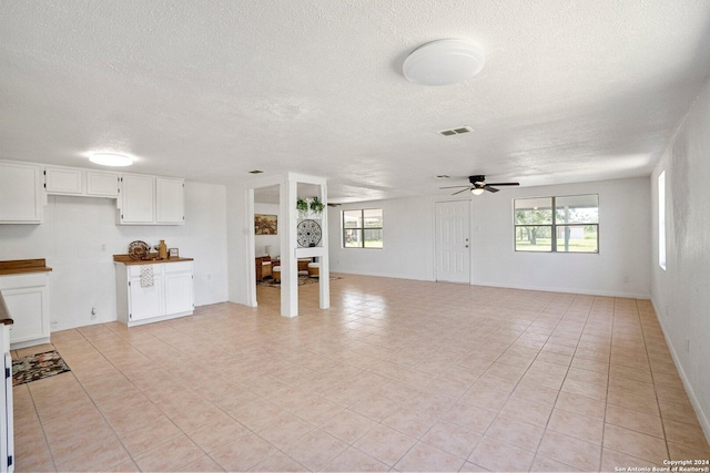 unfurnished living room with a textured ceiling, visible vents, a wealth of natural light, and ceiling fan