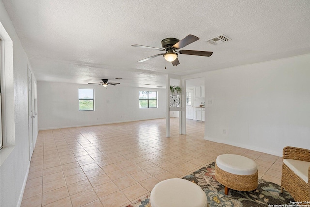 interior space featuring visible vents, baseboards, light tile patterned floors, a textured ceiling, and a ceiling fan