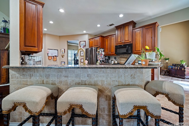 kitchen with a kitchen bar, light hardwood / wood-style floors, stone countertops, stainless steel refrigerator, and kitchen peninsula