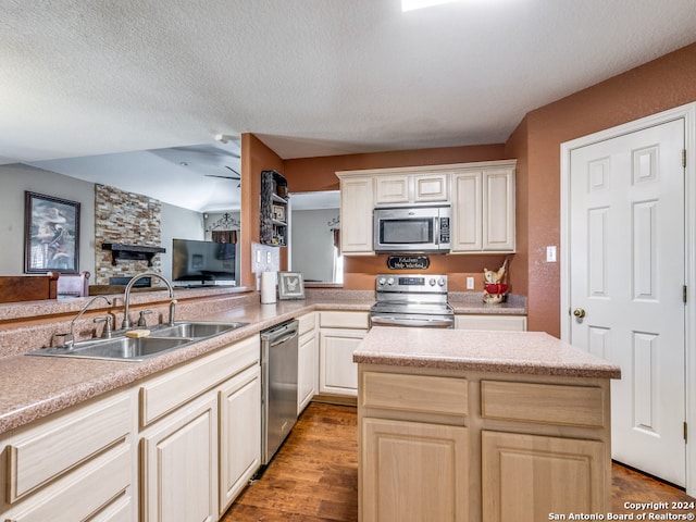 kitchen with sink, a stone fireplace, appliances with stainless steel finishes, wood-type flooring, and a textured ceiling