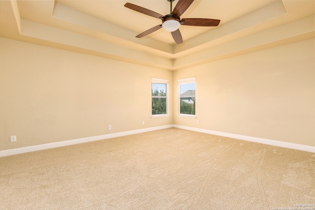 carpeted spare room with ceiling fan and a tray ceiling