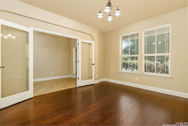 unfurnished room featuring a notable chandelier, hardwood / wood-style flooring, and french doors