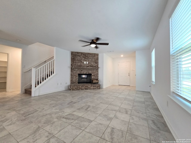 unfurnished living room featuring ceiling fan, light tile patterned floors, brick wall, and a brick fireplace