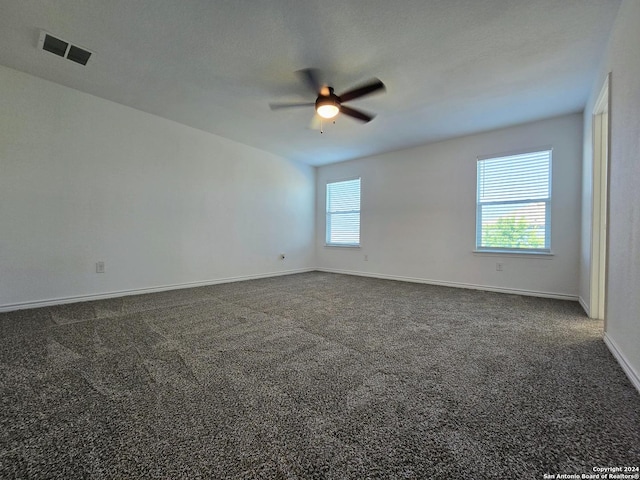 spare room featuring dark colored carpet, plenty of natural light, visible vents, and baseboards