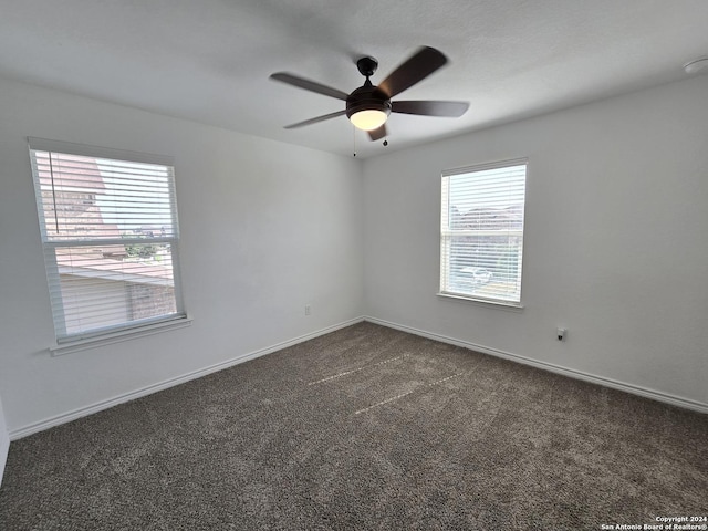 spare room with a ceiling fan, dark colored carpet, and baseboards