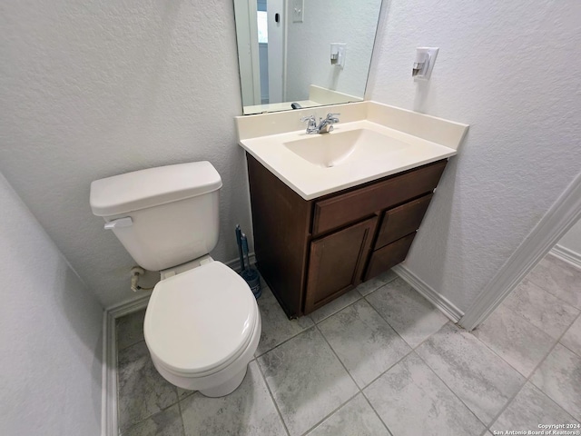 half bath with toilet, a textured wall, and vanity