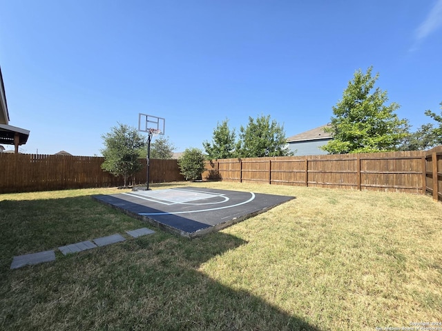 view of sport court featuring a fenced backyard, a lawn, and basketball hoop