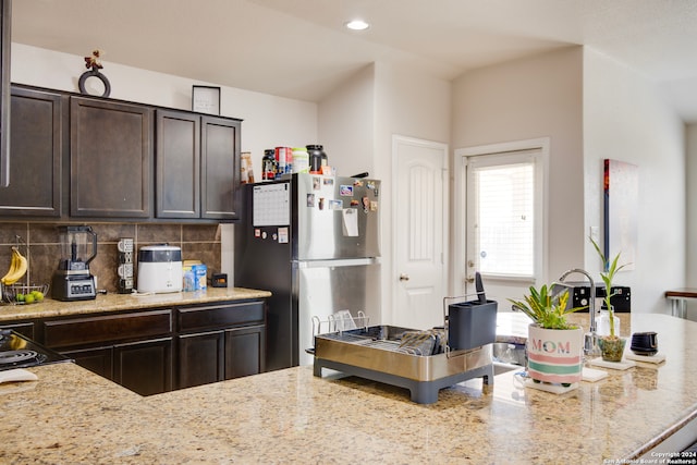 kitchen with light stone counters, dark brown cabinets, tasteful backsplash, and stainless steel refrigerator