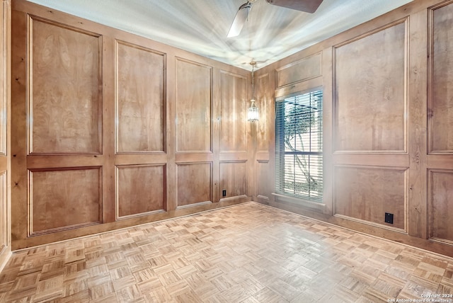 spare room with ceiling fan, wooden walls, and light parquet floors