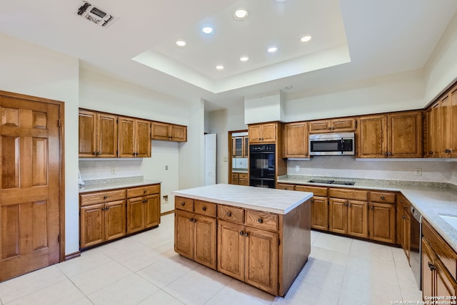 kitchen with decorative backsplash, black appliances, a tray ceiling, a center island, and light tile patterned flooring