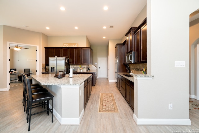 kitchen with appliances with stainless steel finishes, backsplash, light wood-type flooring, light stone countertops, and ceiling fan