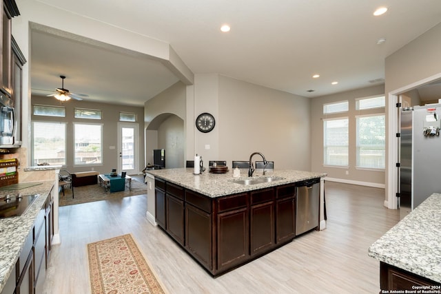 kitchen with an island with sink, light stone counters, appliances with stainless steel finishes, open floor plan, and a sink