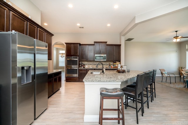 kitchen featuring stainless steel appliances, a breakfast bar, a sink, backsplash, and an island with sink