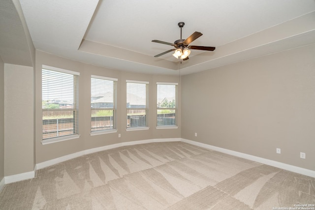 unfurnished room featuring baseboards, a raised ceiling, a ceiling fan, and light colored carpet