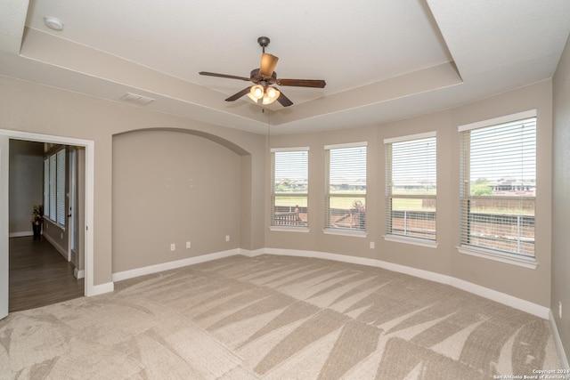 unfurnished room with a tray ceiling, carpet, a ceiling fan, and baseboards