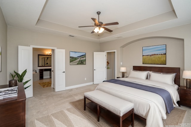 bedroom featuring light colored carpet, a raised ceiling, ensuite bath, and ceiling fan