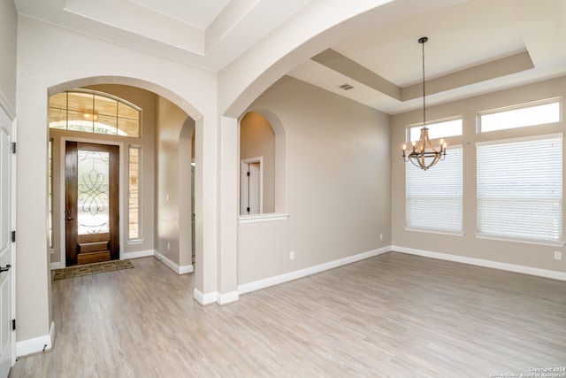 entrance foyer with a notable chandelier, light hardwood / wood-style flooring, a healthy amount of sunlight, and a tray ceiling