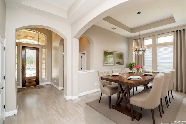 dining area featuring light wood-type flooring, a raised ceiling, a notable chandelier, and plenty of natural light