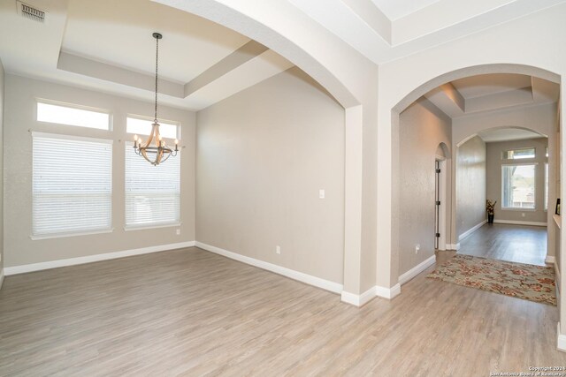 unfurnished room with a notable chandelier, a raised ceiling, and light hardwood / wood-style floors