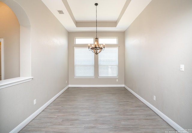 unfurnished dining area featuring a tray ceiling, arched walkways, a notable chandelier, visible vents, and baseboards