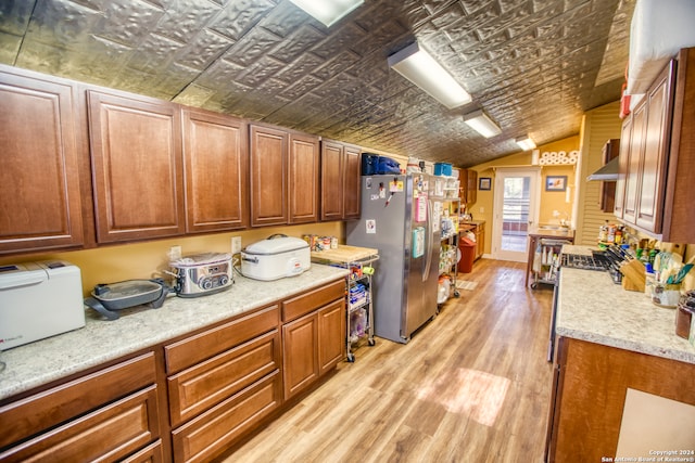 kitchen with brick ceiling, wall chimney exhaust hood, stainless steel refrigerator, light wood-type flooring, and lofted ceiling