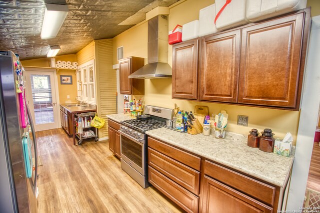 kitchen featuring wall chimney exhaust hood, vaulted ceiling, light hardwood / wood-style floors, and stainless steel appliances