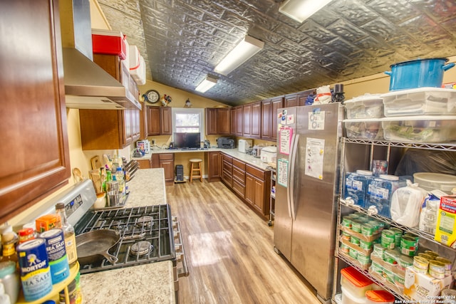 kitchen featuring light wood-type flooring, wall chimney exhaust hood, vaulted ceiling, stainless steel fridge, and stove