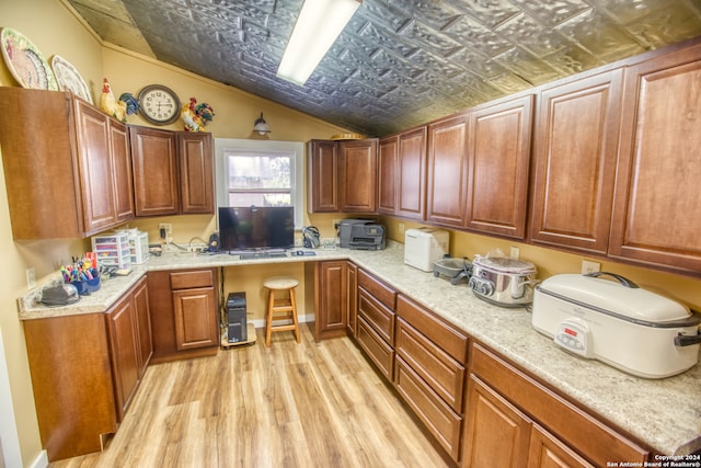 kitchen with light stone counters, lofted ceiling, light wood-type flooring, and built in desk