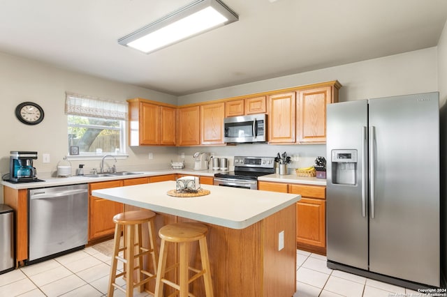 kitchen featuring appliances with stainless steel finishes, sink, a kitchen island, light tile patterned flooring, and a breakfast bar