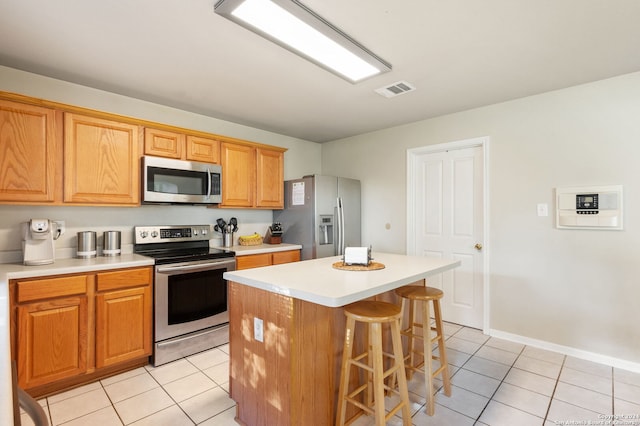 kitchen featuring a kitchen island, stainless steel appliances, light tile patterned floors, and a kitchen bar