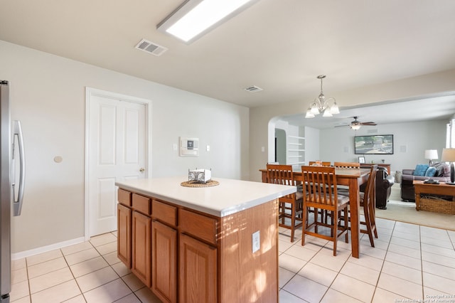 kitchen featuring light tile patterned flooring, a center island, decorative light fixtures, ceiling fan with notable chandelier, and stainless steel refrigerator