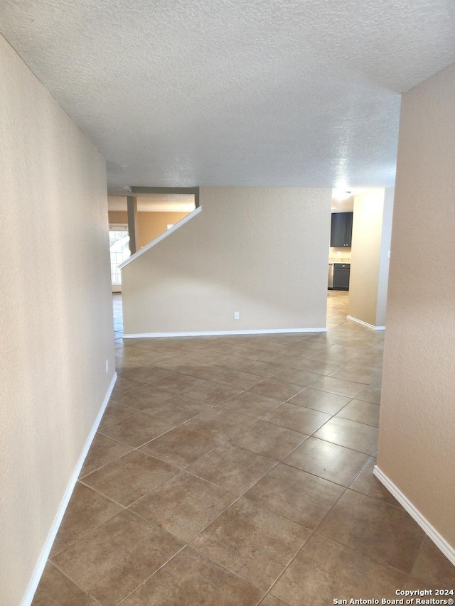 unfurnished room with a textured ceiling, tile patterned floors, and baseboards