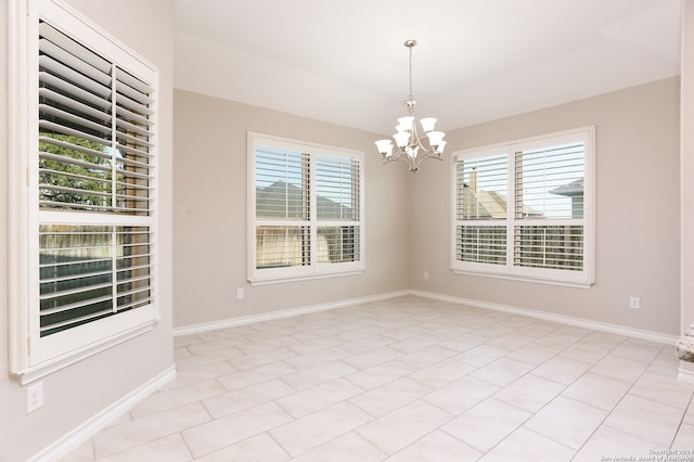 empty room with a notable chandelier, light tile patterned floors, and a wealth of natural light